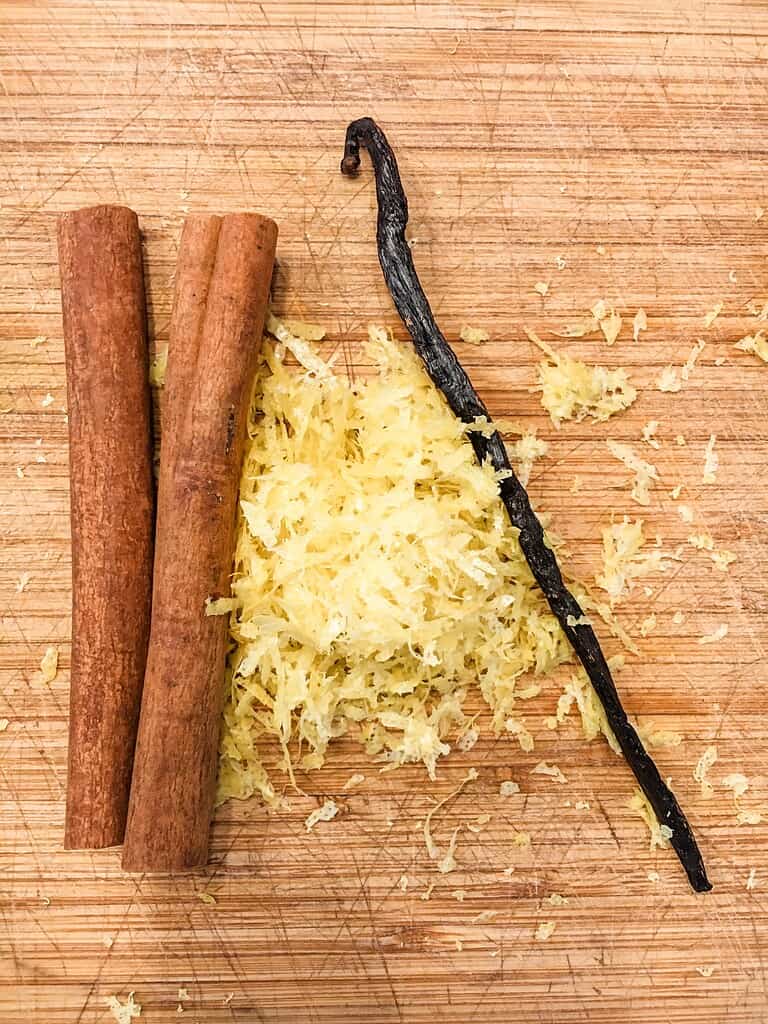 Cinnamon sticks, lemon zest, and vanilla bean on a chopping board.