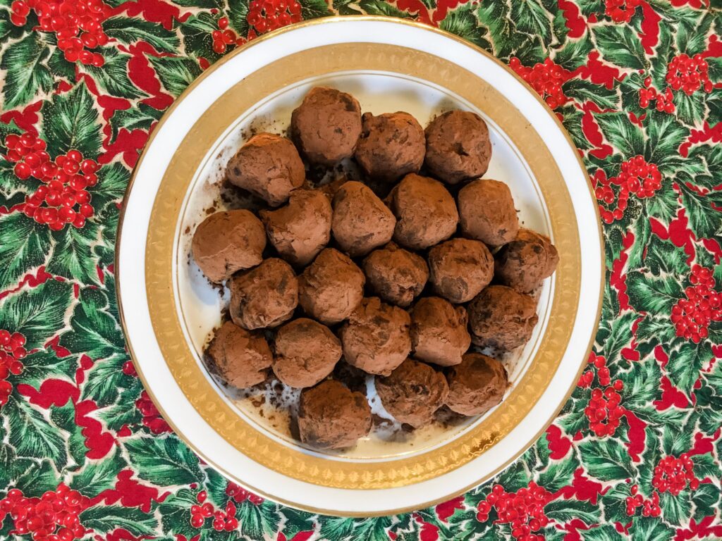 Chocolate truffles on a gold rimmed plate on top of a Christmas table cloth.