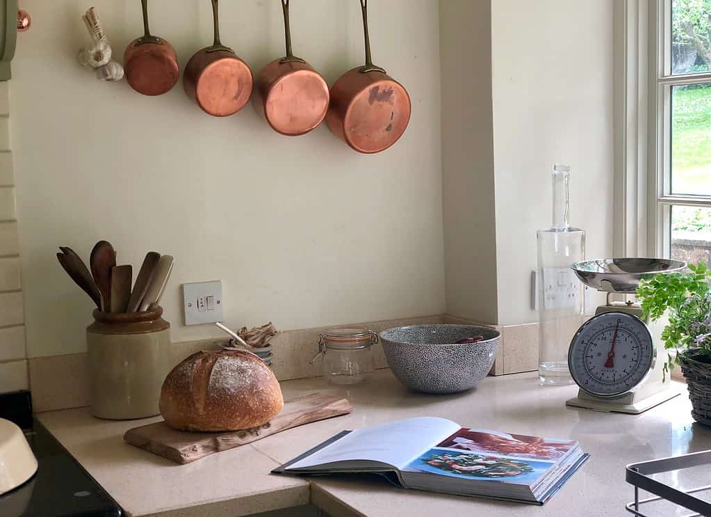 Copper pots hanging on a wall next to a cookbook in a kitchen