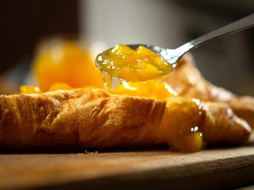 jam being placed on a croissant with spoon