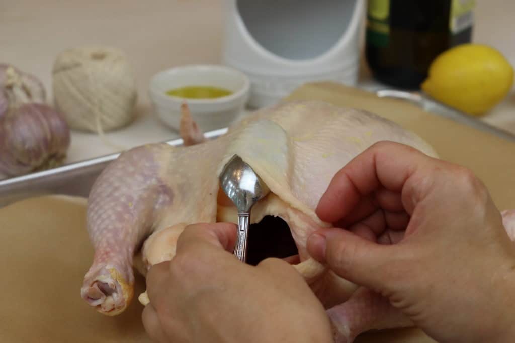 Hands using a spoon to separate the chicken skin from the breast of the chicken