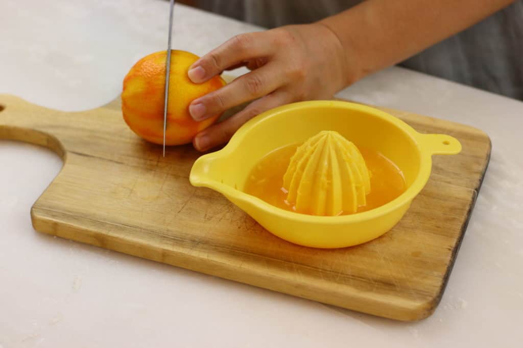 Hand holding an orange while slicing it next to a juicer.