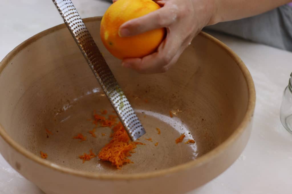 Hands zesting an orange into a large bowl.