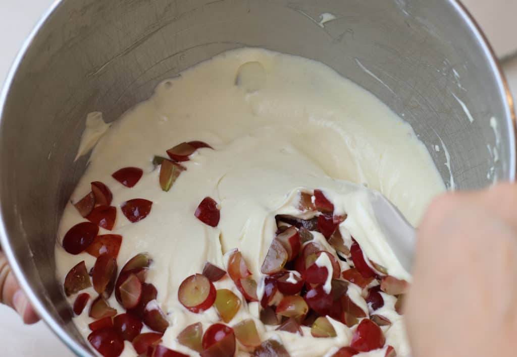 Chopped grapes being folded into cake batter with a spatula.