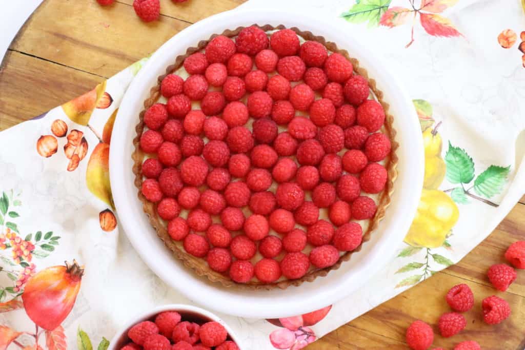 Raspberry tart on a colorful towel over a cutting board.