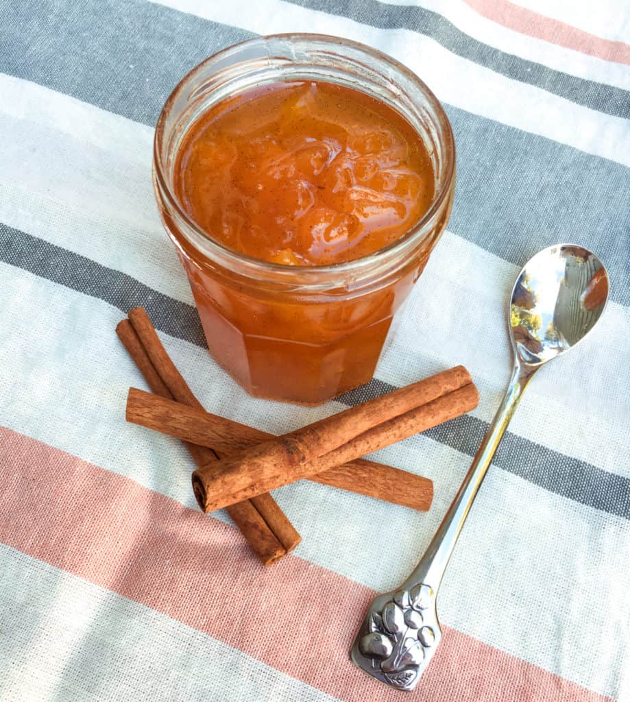 Opem Jar of jam on a striped tablecloth with cinnamon sticks and spoon next to it.