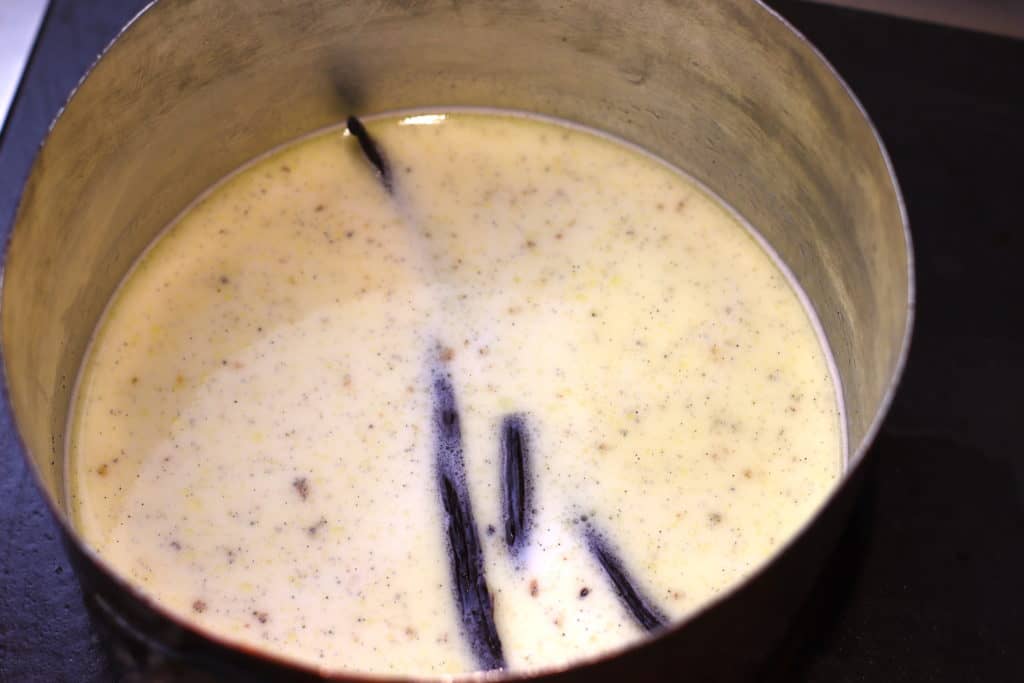 Medium saucepan with milk mixture and vanilla beans inside.