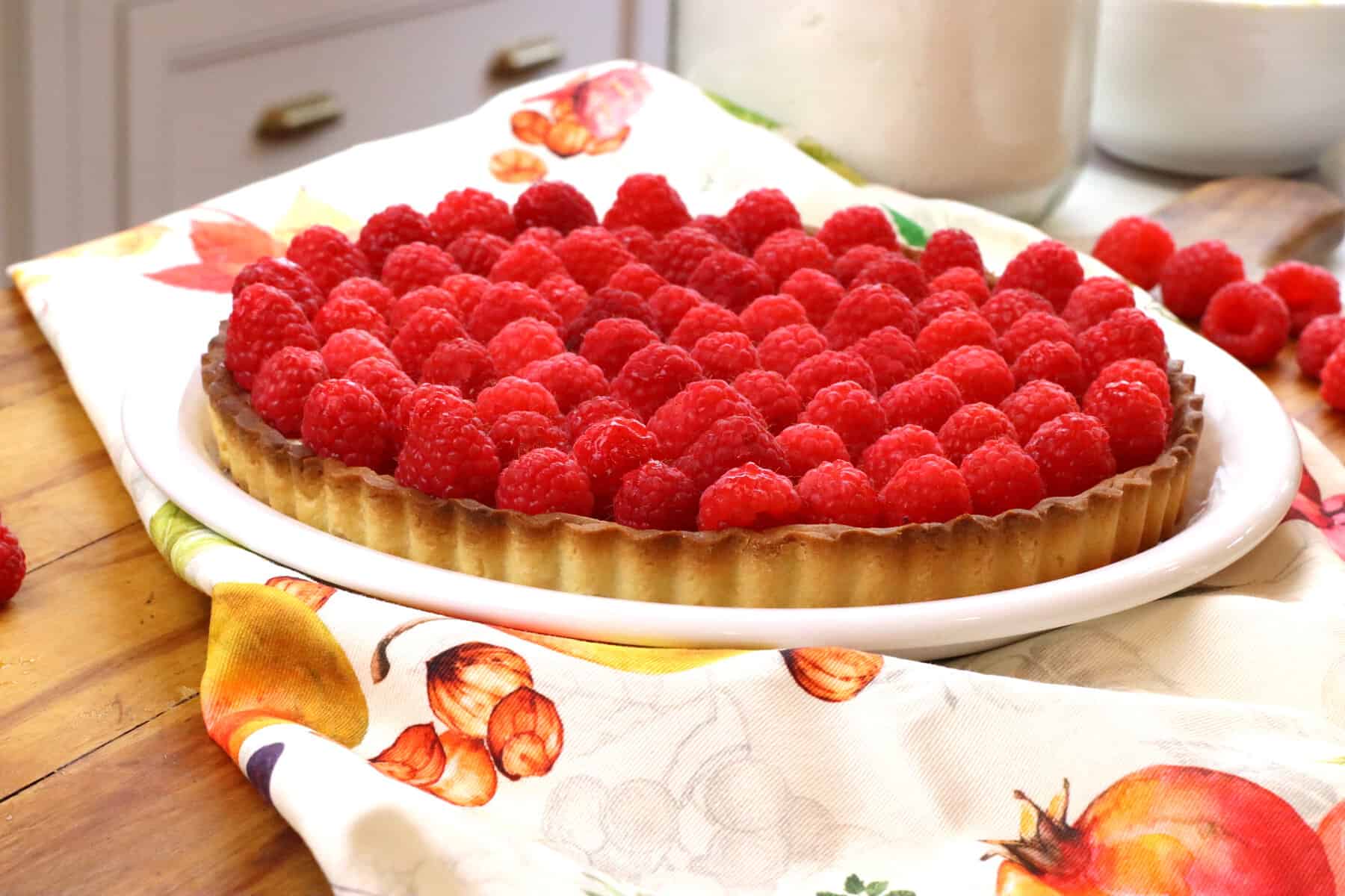 Raspberry tart on top of a plate with a colorful towel.