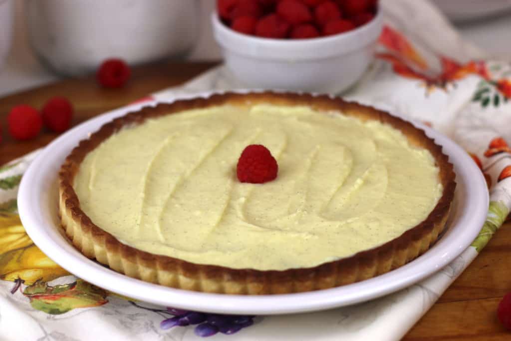 Tart shell filled with pastry cream with one raspberry on top.