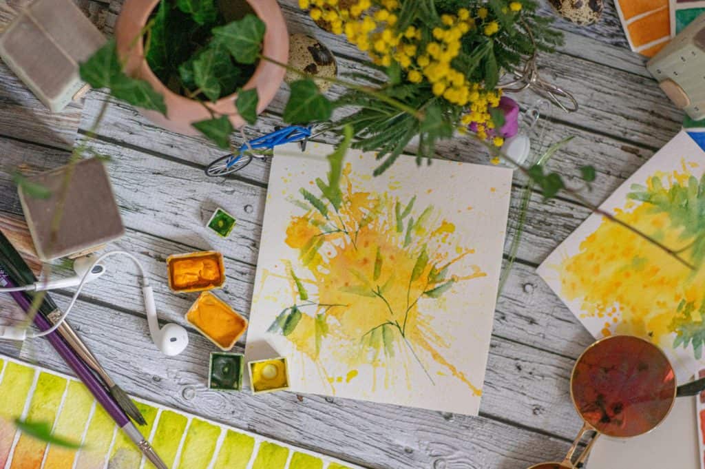 Painting of yellow flowers next to yellow flowers, paint, and brushes