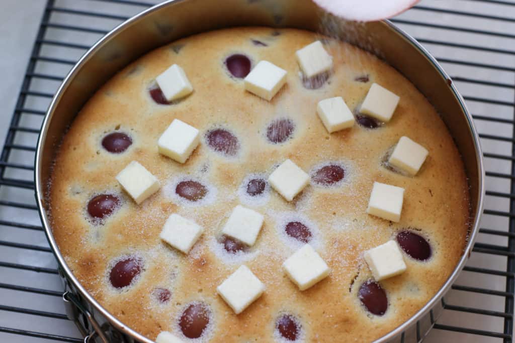 Grape cake with cubes of butter on top, being sprinkled with sugar