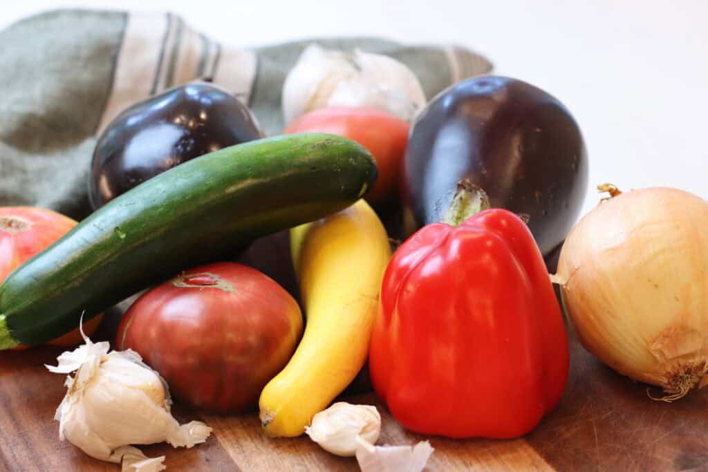 A pile of various fresh produce on a cutting board that is used to make ratatouille.