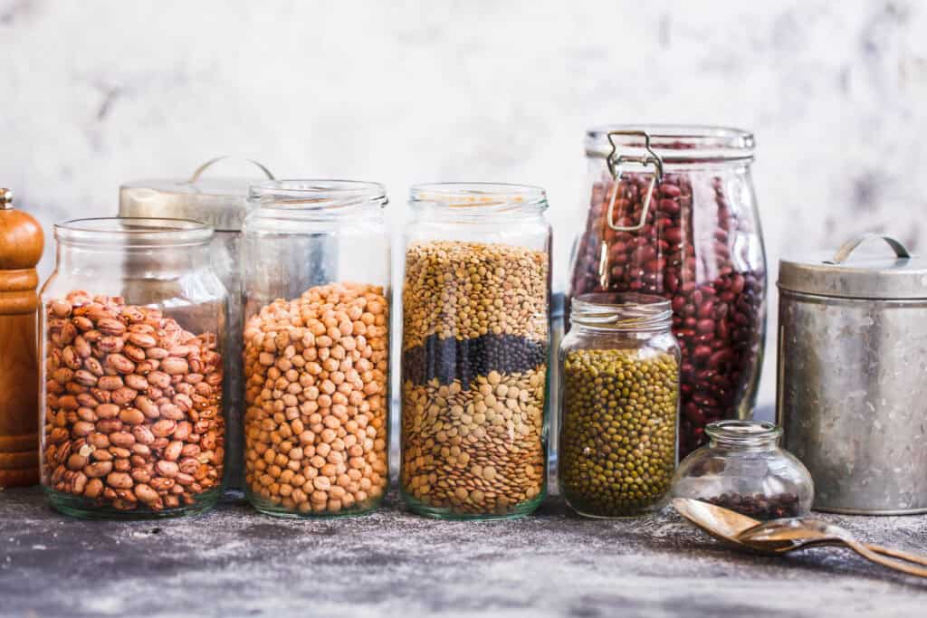 Colorful glass jars filled with various dried legumes and grains, showcasing rustic French kitchen decor and organic pantry storage.