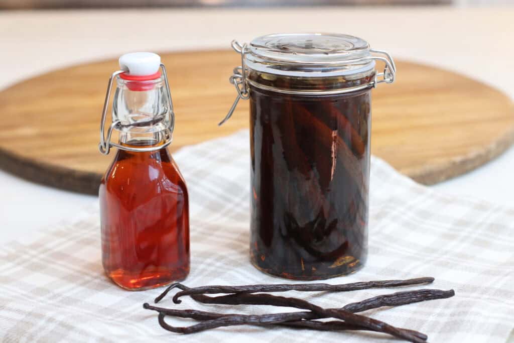 A small bottle of homemade vanilla extract next to a large clear jar filled with vanilla beans and homemade vanilla extract.