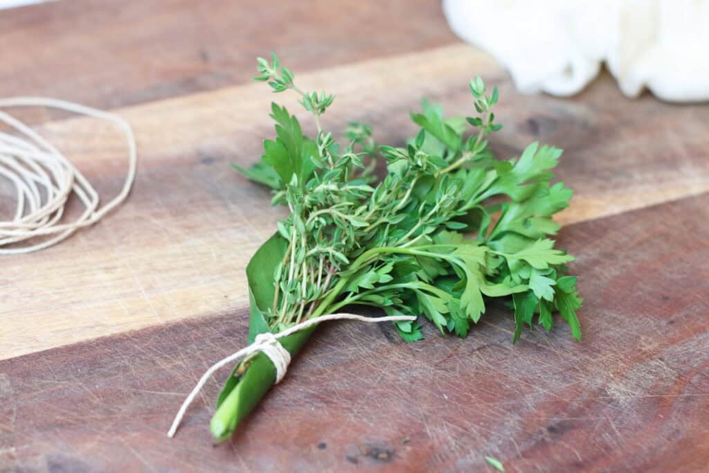 Bundle of herbs tied with kitchen twine sitting on a cutting board