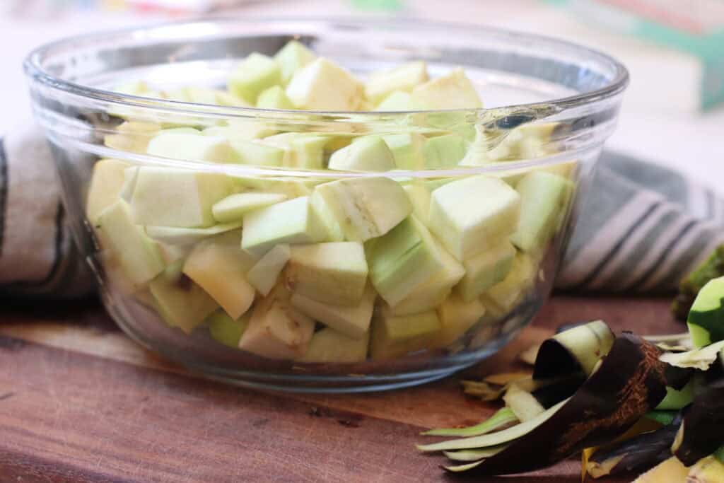 Glass bowl filled with diced eggplant and squash, sitting on a cutting board.