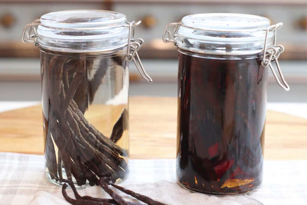 Two clear jars next to each other.  One is filled with clear vodka and vanilla beans.  The other jar is filled with homemade vanilla extract and vanilla beans.