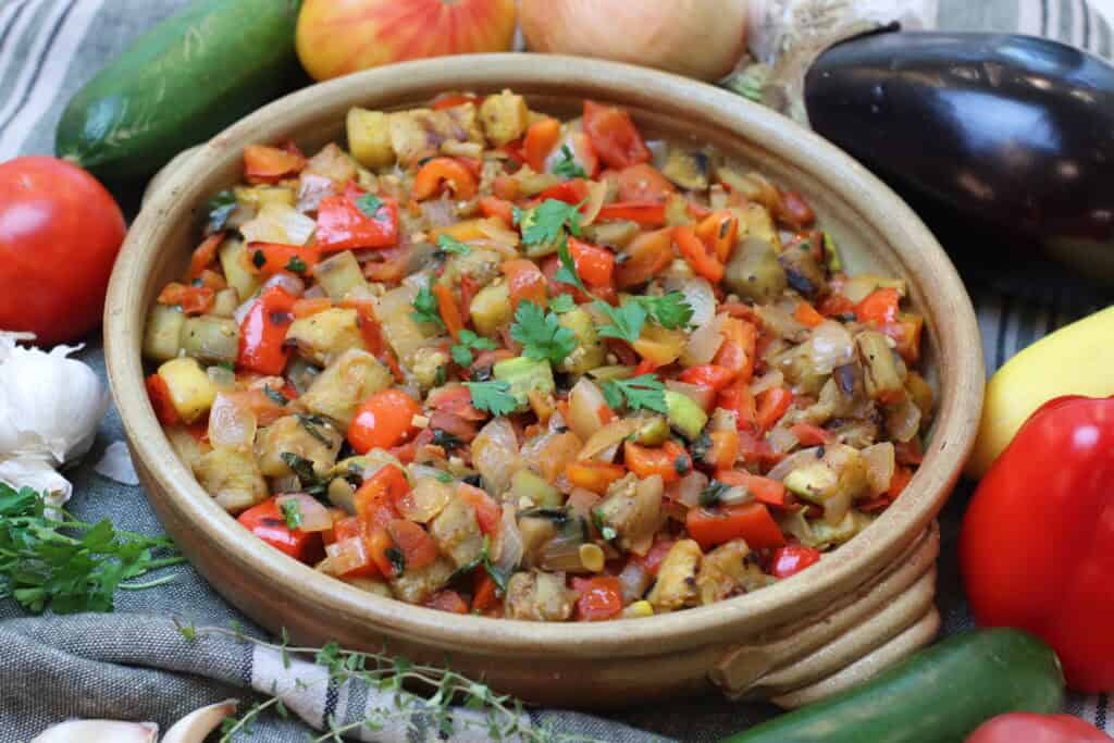 Close up picture of ratatouille in a rustic dish, surrounded by fresh produce.
