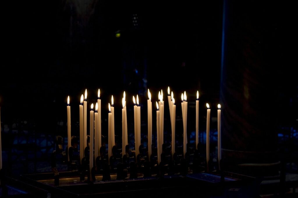 Softly glowing white candles in a dark setting, creating a warm, peaceful ambiance. Ideal for remembering loved ones on La Toussaint.