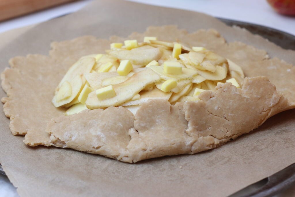 Buttery pastry dough topped with sliced apples and white chocolate pieces, ready to be baked into a delicious French-inspired dessert.