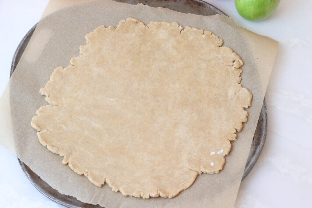 Fresh galette dough rolled out and placed on a piece of parchment paper directly on a baking sheet.