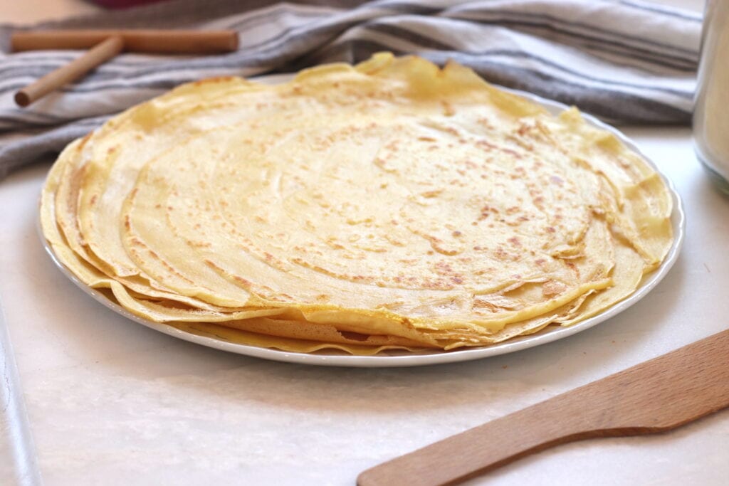 Flaky French crêpes on a white platter, perfect for a quaint French living breakfast or gouter setting.