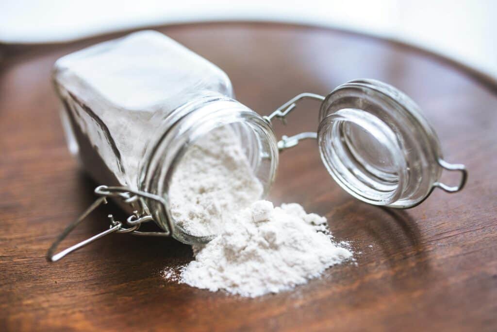 Jar of American flour overturned on a wooden board with flour spilling out.