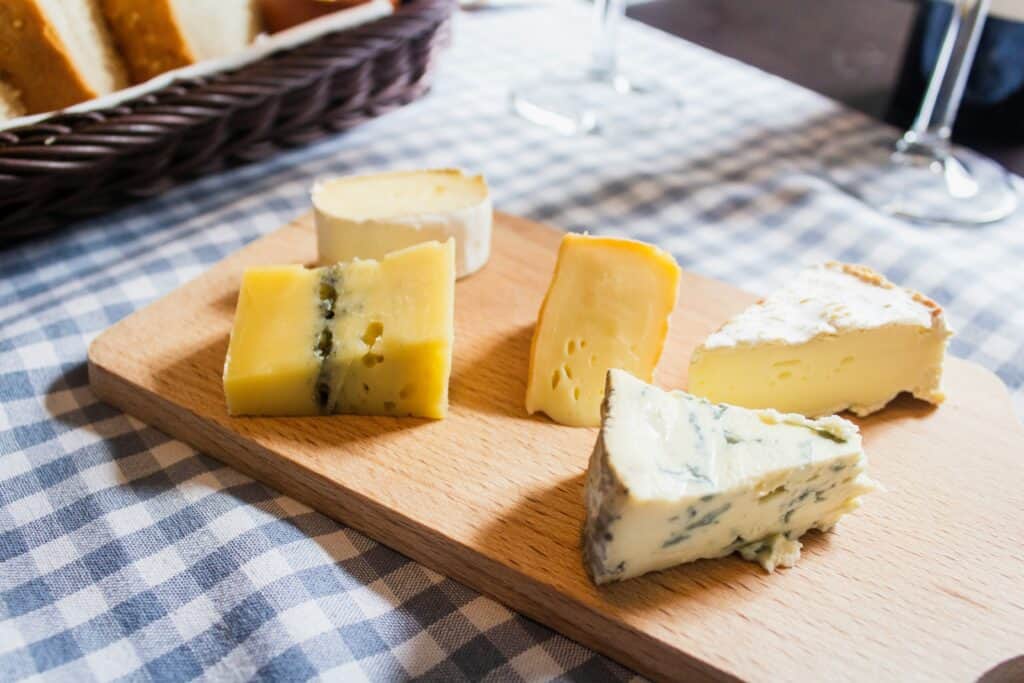 Assorted cheeses on a wooden board with a blue checkered tablecloth for a cozy French lifestyle setting.