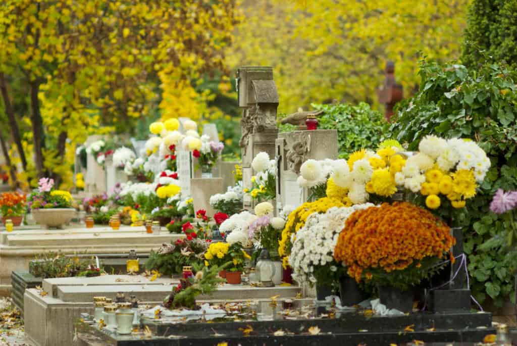 Vibrant autumn cemetery with colorful flowers and ornate headstones, evoking peaceful remembrance in a scenic French garden setting.