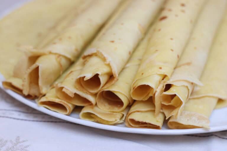 Golden crepes stacked on a white plate, ready to be served as part of authentic French cuisine. Perfect for breakfast, dessert, or savory fillings, showcasing traditional French culinary delights.
