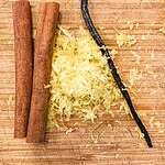 Cinnamon sticks, lemon zest, and vanilla bean on a chopping board.