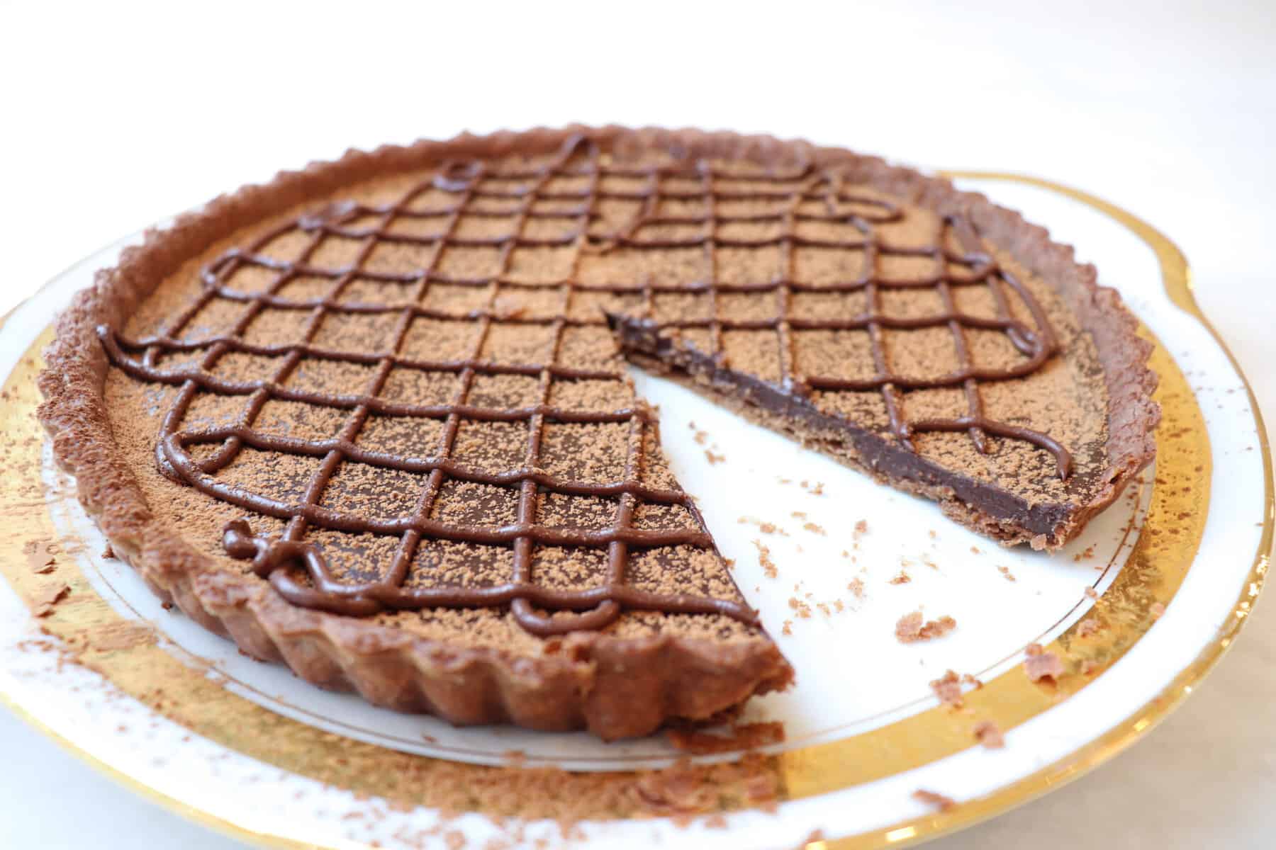 French chocolate tart dusted with cocoa sitting on a white plate with gold border