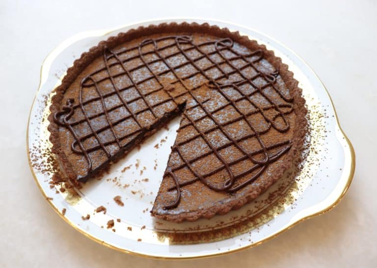 Classic French chocolate tart with a slice missing sitting on a plate