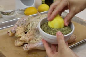 Hand dipping half of a lemon in a bowl of herbes de Provence.