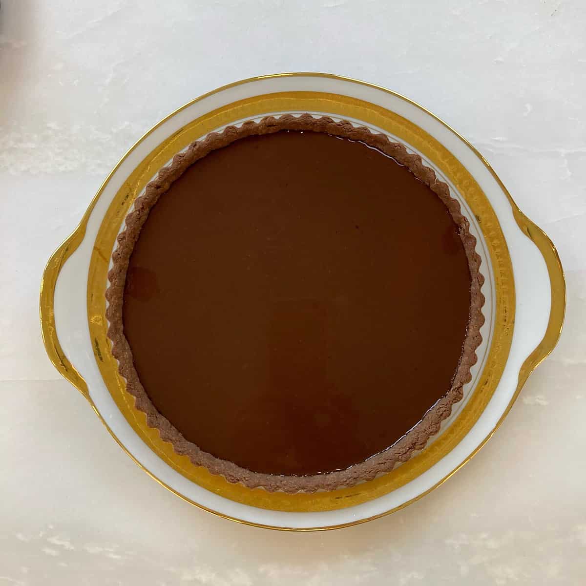 Chocolate tart shell filled with chocolate ganache on a white and gold plate