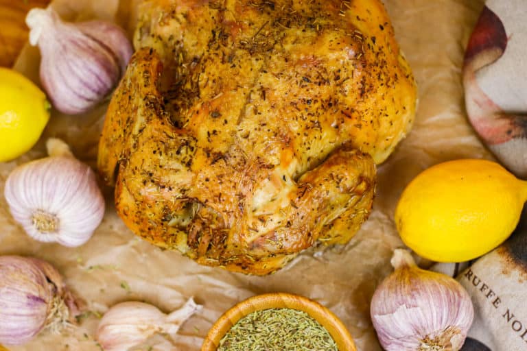 Roasted chicken on a piece of parchment paper surrounded by lemons, garlic and herbs