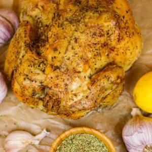 Roasted chicken on a piece of parchment paper surrounded by lemons, garlic and herbs