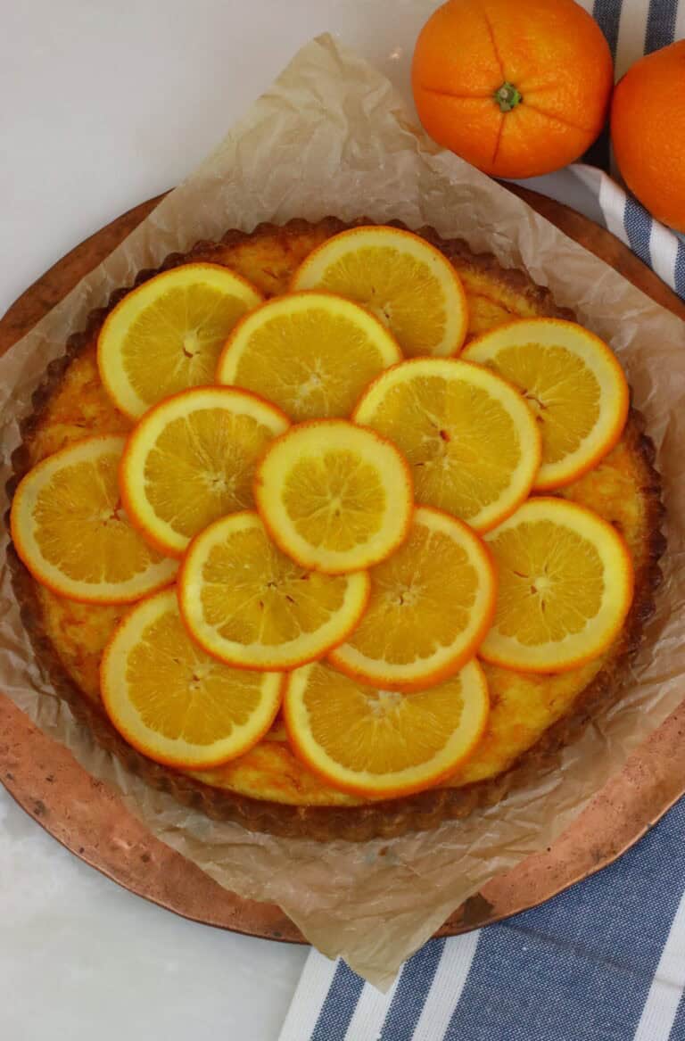 Juicy orange upside-down cake topped with fresh orange slices, displayed on parchment paper on a round wooden serving board.
