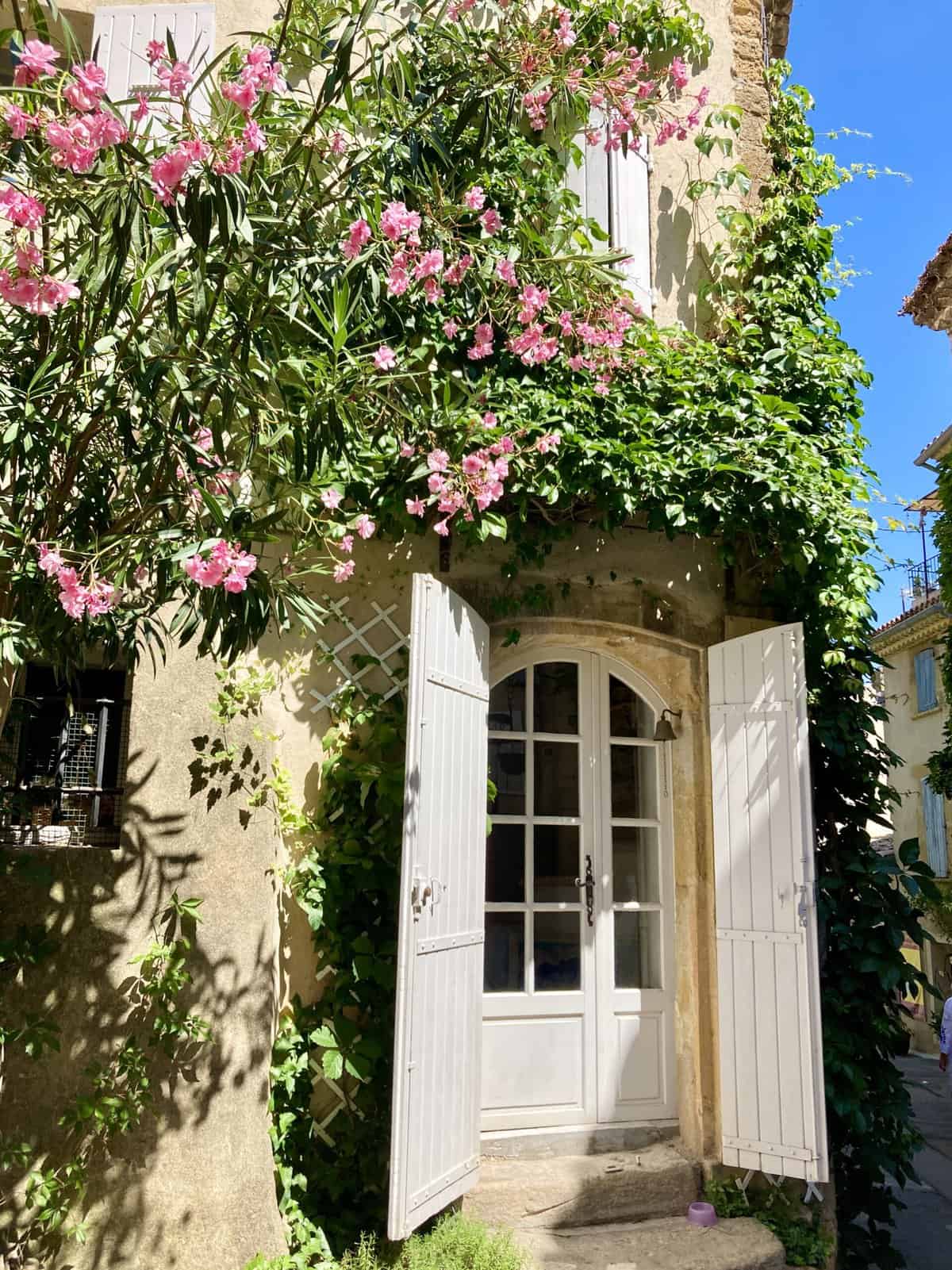 A white door on a Provencal home surrounded by blooming pink flowers