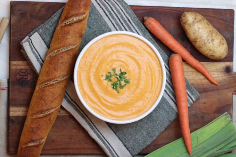 Overhead view of French potage soup with baguette and carrots surrounding the bowl.