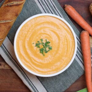 Overhead view of French potage soup with leeks, carrots, and potatoes, as well as a crusty baguette adjacent.