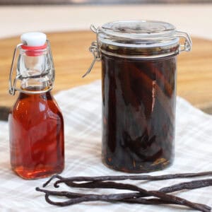 A small bottle of homemade vanilla extract next to a large clear jar filled with vanilla beans and homemade vanilla extract.