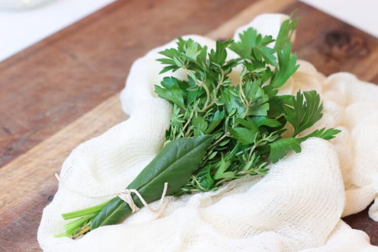 Bundle of herbs sitting on cheesecloth on a wooden board.