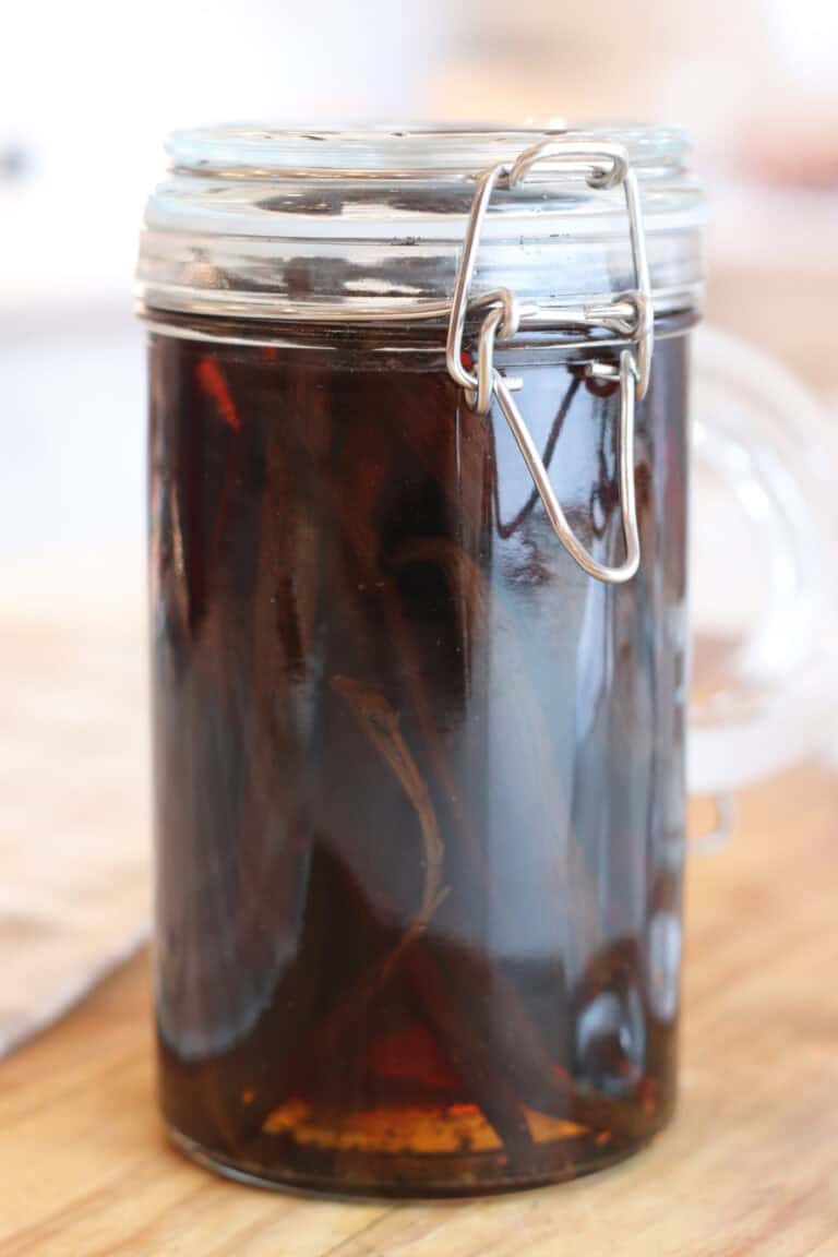 A clear jar filled with vanilla beans, vodka, and homemade vanilla extract sitting on a cutting board.