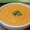 Side view of a white bowl filled with orange French potage soup with parsley garnish on top.