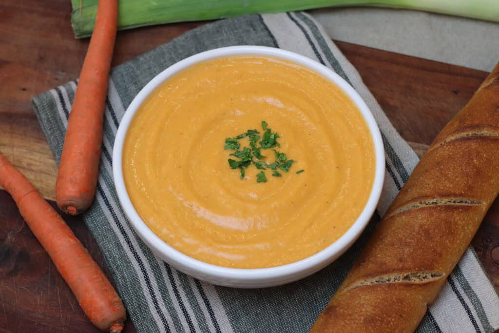 Overhead view of French potage soup with a crusty baguette and carrots next to it.