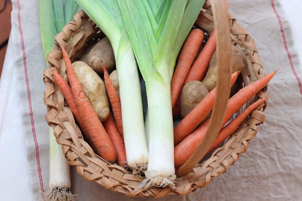Basket with whole leeks, potatoes and carrots inside.