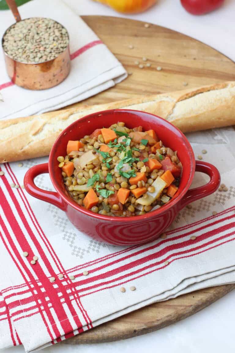 Savory lentil stew with vegetables served in a red dish, accompanied by a baguette on a wooden platter, perfect for cozy French-inspired meals.