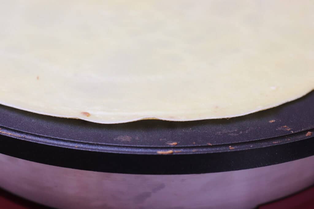 Thin crepe batter cooking on a non-stick skillet, ready to be filled or folded for a French-style dish in a kitchen setting.