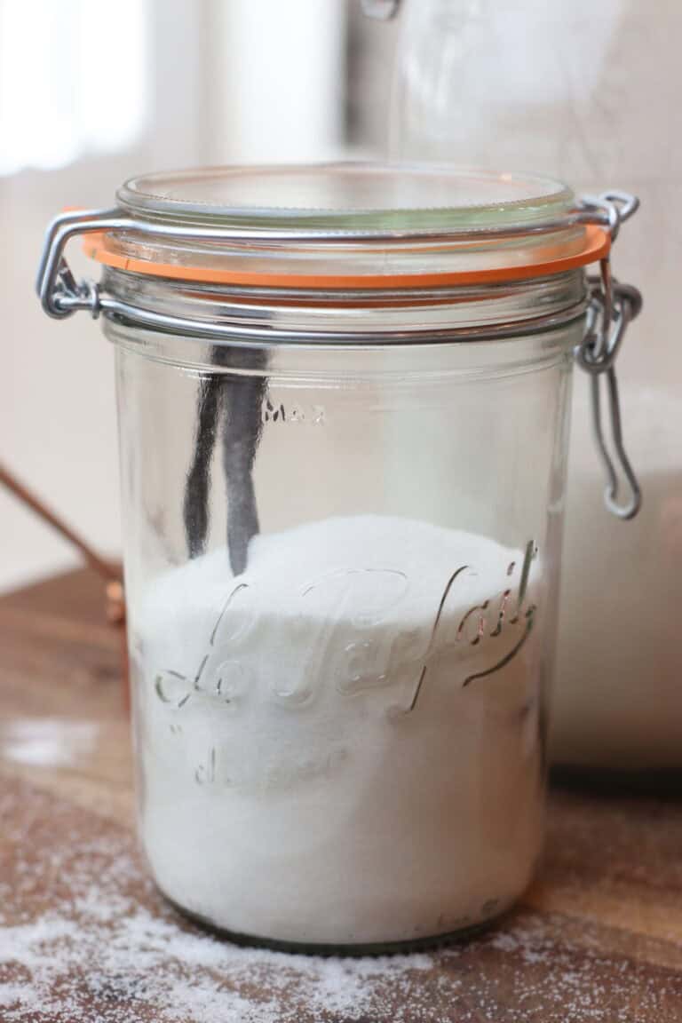 Clear jar of vanilla sugar on a rustic brown cutting board found in a French Farmhouse kitchen.